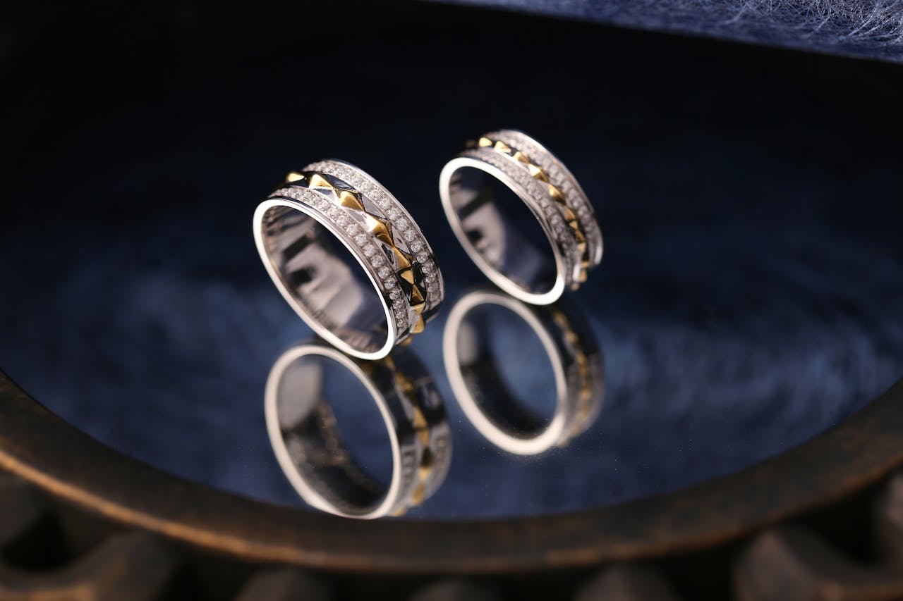 Close-up of elegant silver rings adorned with diamonds reflecting on a dark surface.
